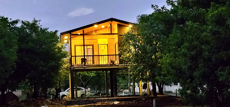 Raised pine house with glowing windows among trees at dusk, by The Wooden Story