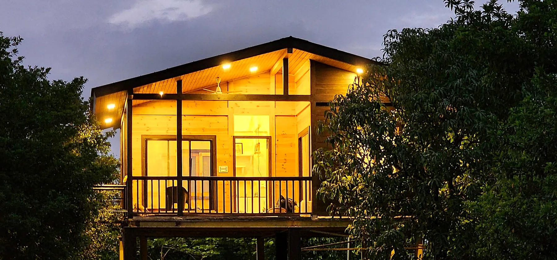 Pine stilt house with glowing windows among trees at dusk, built by The Wooden Story